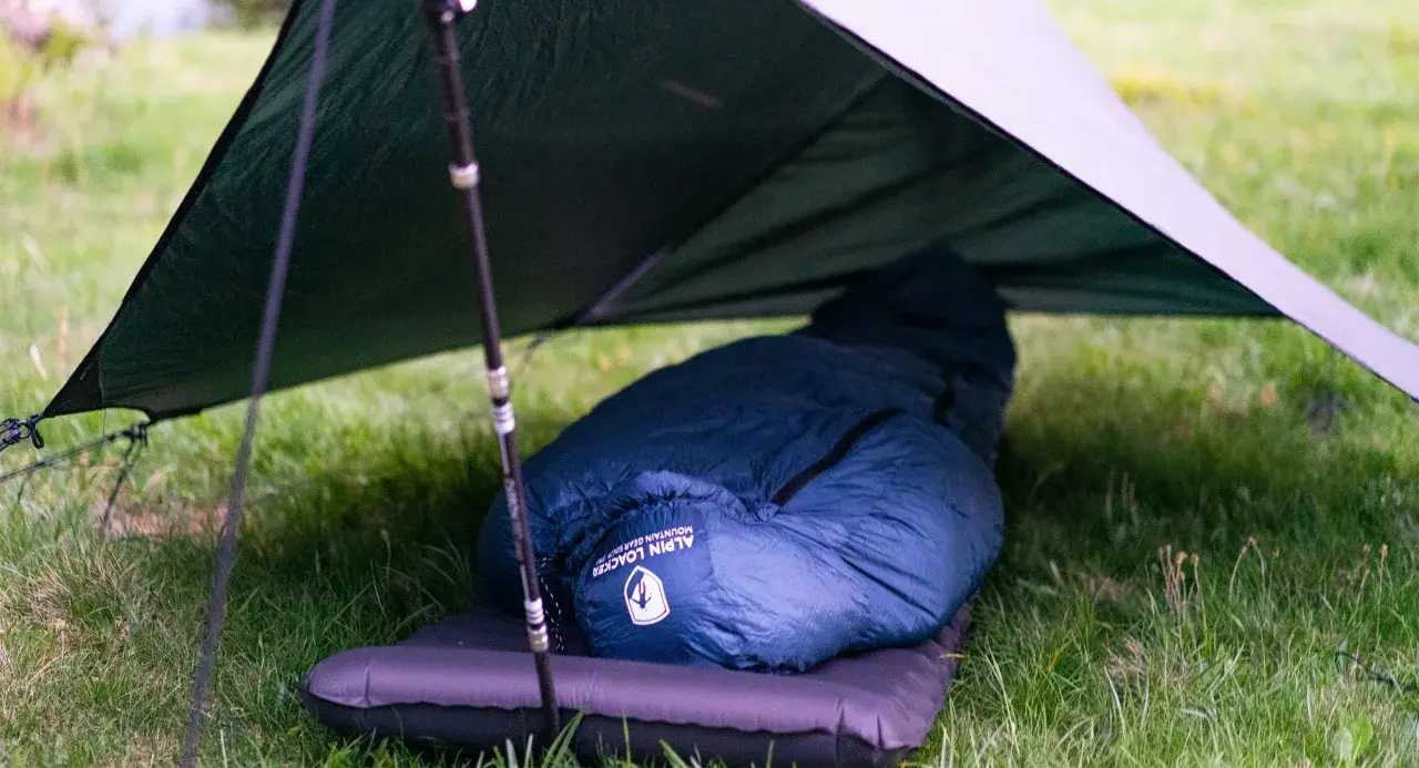 Ein dunkelblauer Kunstfaser-Schlafsack liegt auf einer Isomatte unter einem Tarp. Perfekt für Outdoor-Abenteuer, auch wenn man ihn mal waschen muss.