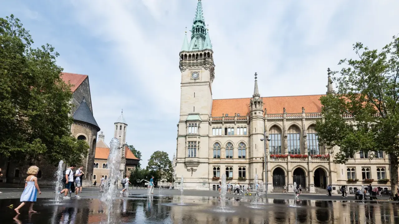 Kinder planschen im Brunnen vor dem Rathaus. Hier kann man in Braunschweig viel erleben, z.B. den Dom besichtigen.