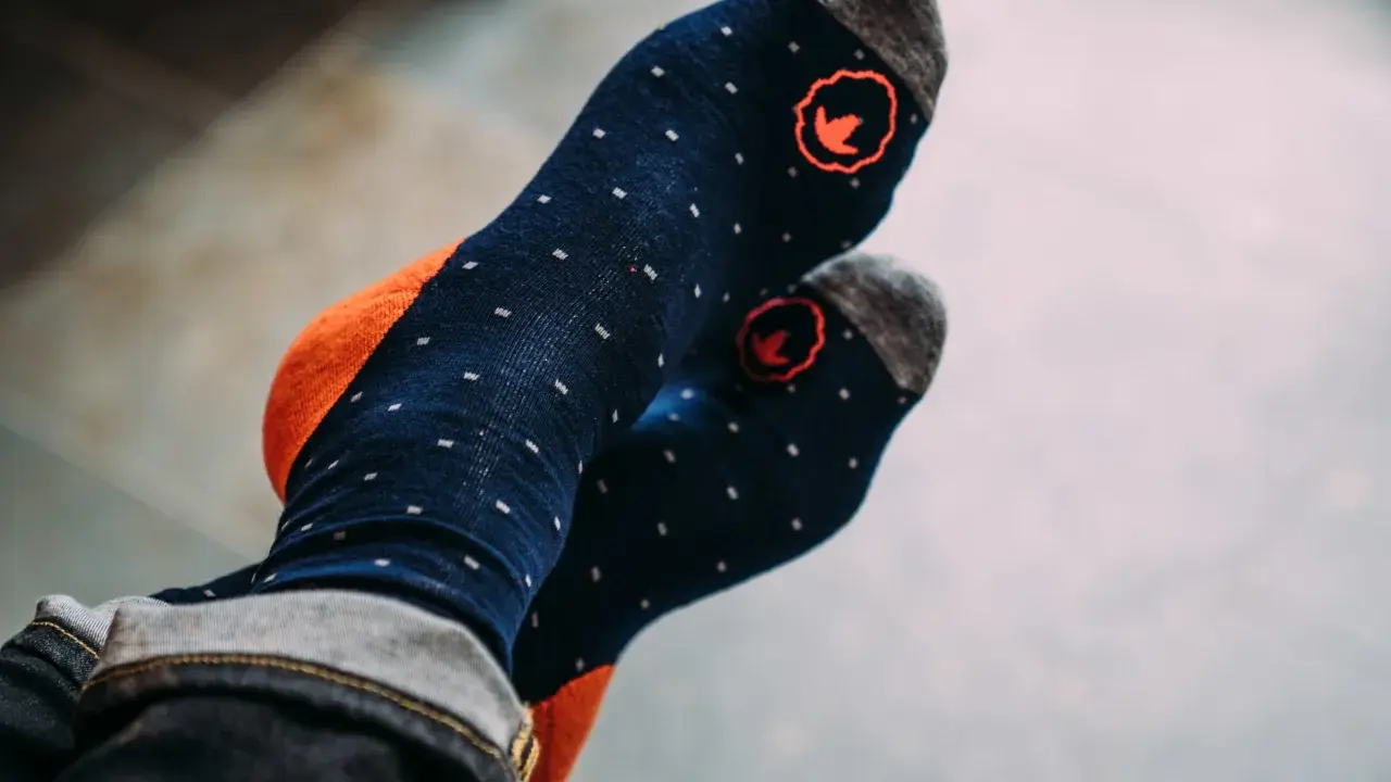 Blaue Socken mit orangen Akzenten und kleinen weißen Punkten. Die Socken haben ein rotes Logo und sind aus Merinowolle, ideal zum Waschen.