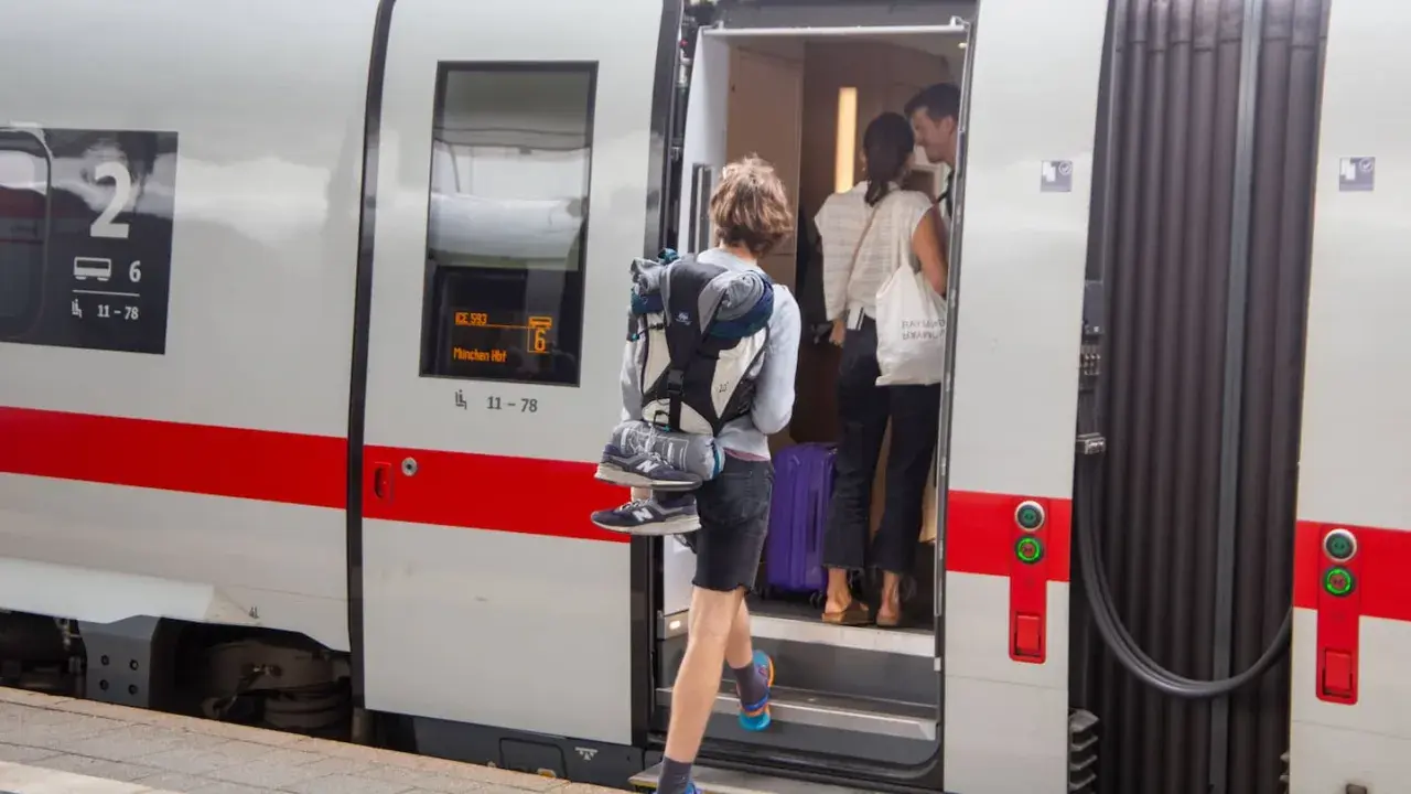 Reisende steigen in den ICE ein, um die ICE strecken zu befahren. Ein junger Mann mit Rucksack und Schuhen am Gepäck steigt als Erster ein.