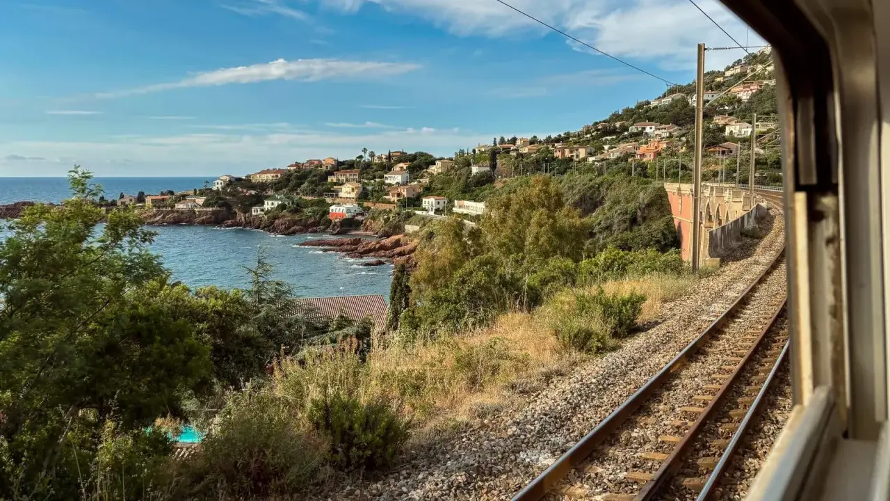 Blick aus dem Fenster eines Nachtzugs Paris Nizza auf eine Küstenlandschaft mit Häusern, Meer und Bahngleisen.