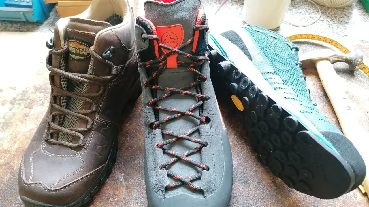 Drei Wanderschuhe von verschiedenen Herstellern: braun, grau und türkis. Werkzeuge und Garn liegen daneben.