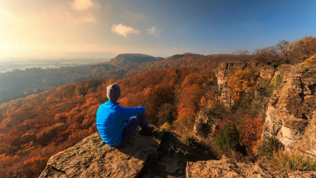 Ein Wanderer genießt den Ausblick auf die herbstliche Landschaft Norddeutschlands von einem Felsvorsprung.