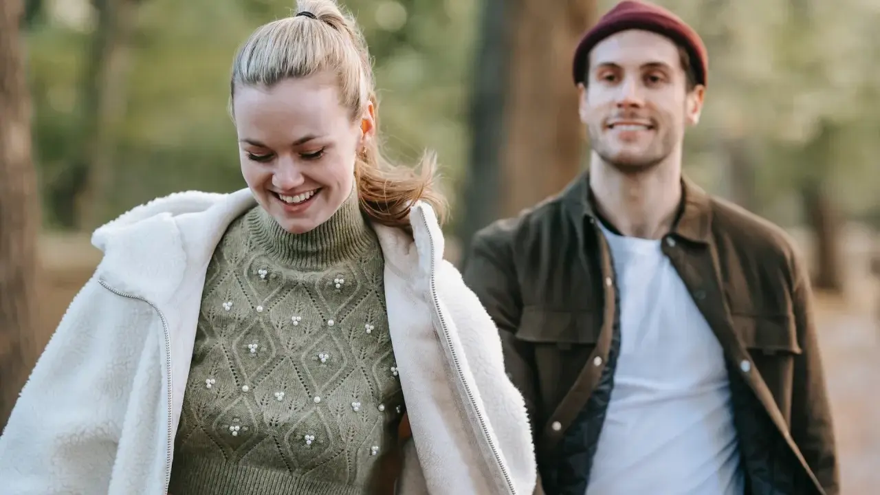 Ein lächelndes Paar im Freien. Sie trägt einen Strickpullover und eine Lammfelljacke, er eine Jacke und Mütze. Perfekt, um was anziehen bei 15 Grad.
