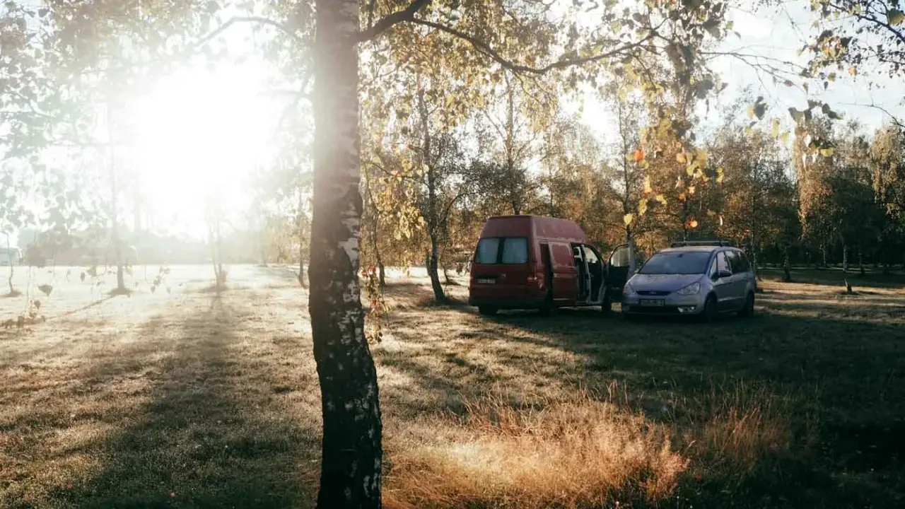 Sonnenaufgang im Herbst. Ein roter Camper und ein silberner Van stehen auf einer Wiese. Das ist Freiheit, das ist was ist wildcampen.