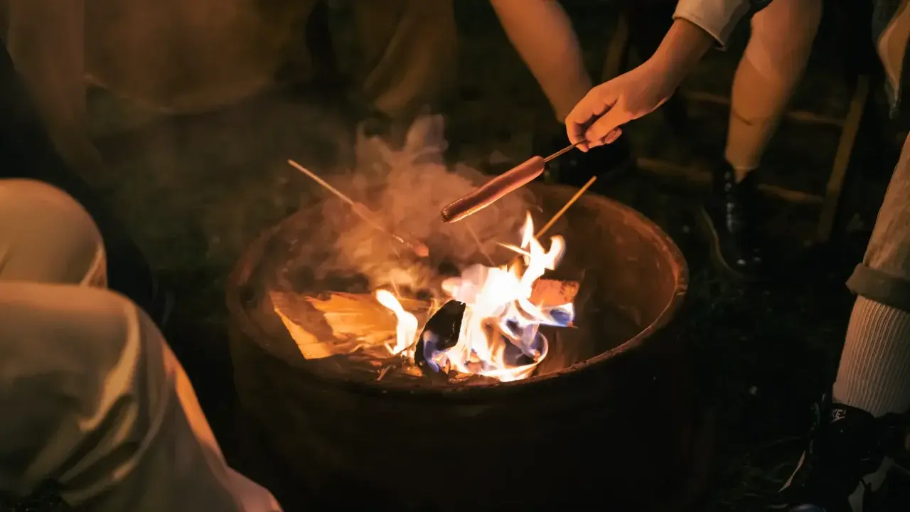 Kinder machen Feuer und rösten Würstchen über der Flamme.