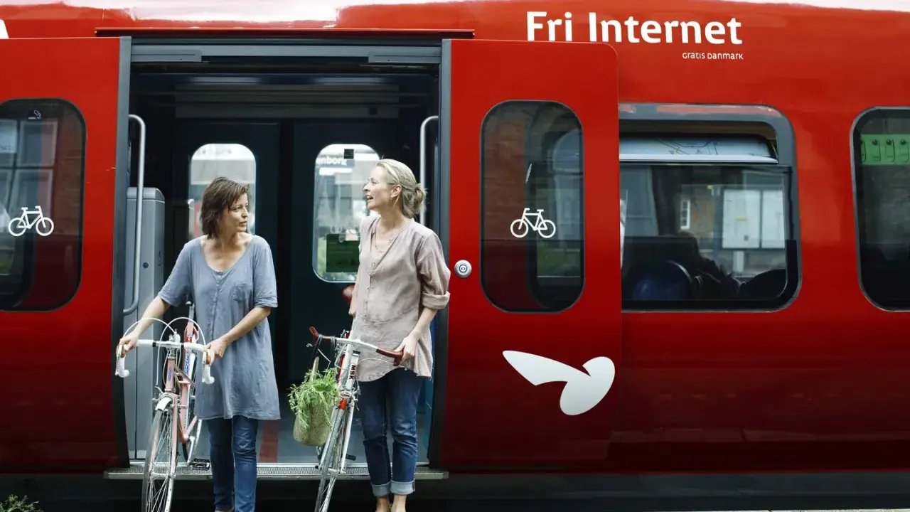 Zwei Frauen mit Fahrrädern steigen in einen roten **denmark train** nach Kopenhagen.
