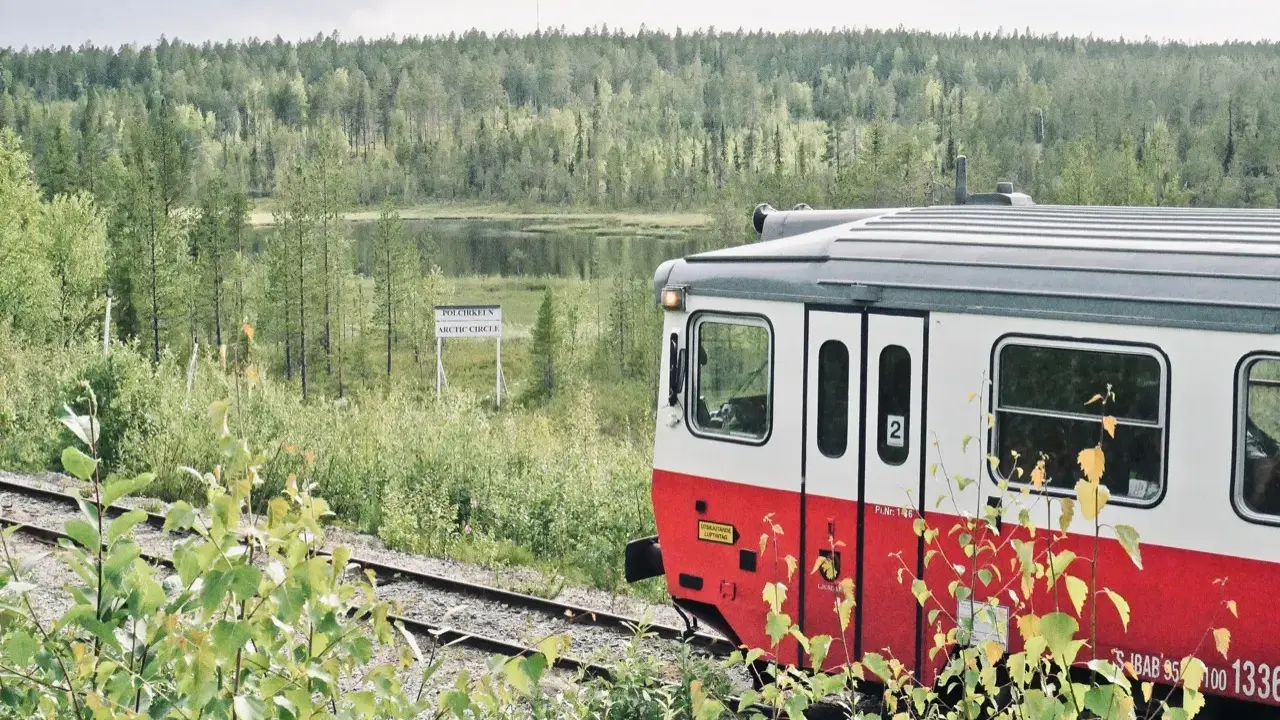 Roter und weißer schwedischer Zug fährt durch eine üppige Landschaft mit einem Schild "Arctic Circle".