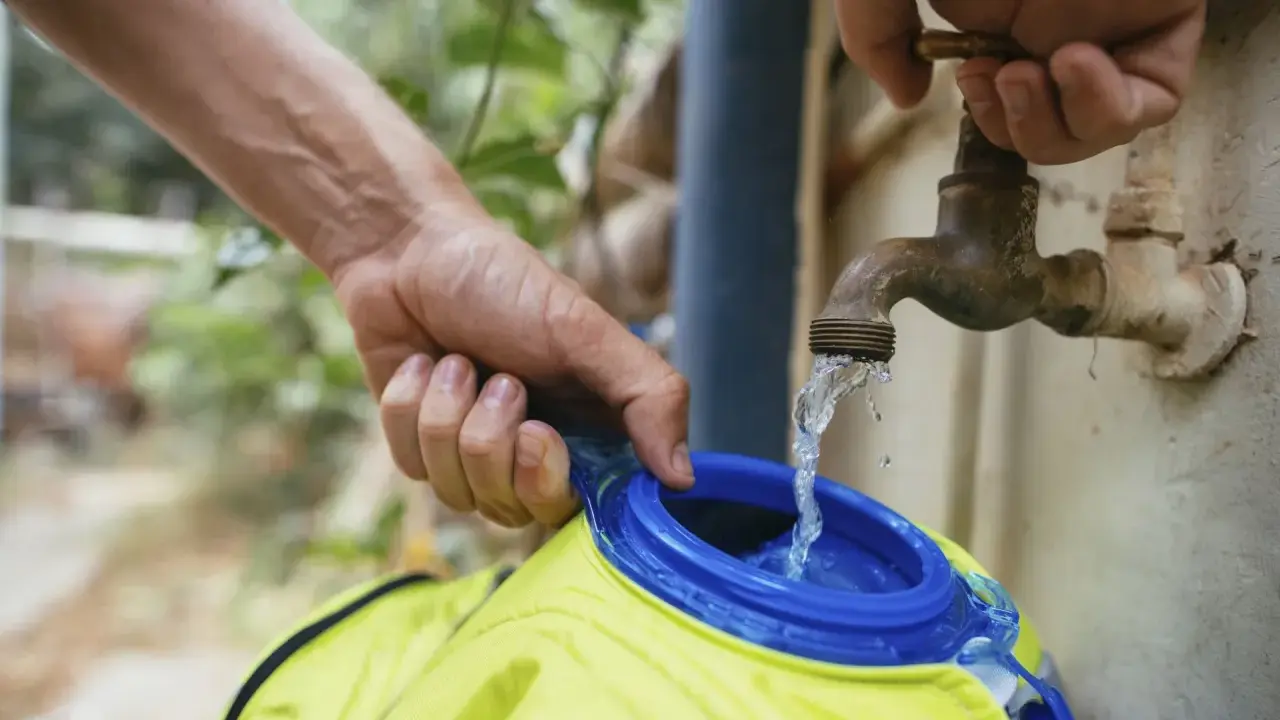 Wasser fließt aus einem alten Wasserhahn in eine gelbe Trinkblase. Nach dem Befüllen muss die Trinkblase trocknen.