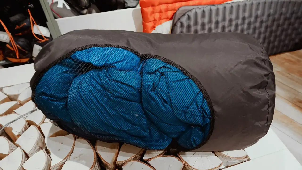 Ein blauer Schlafsack wird in einen dunklen Packsack gestopft, bereit für das nächste Abenteuer.