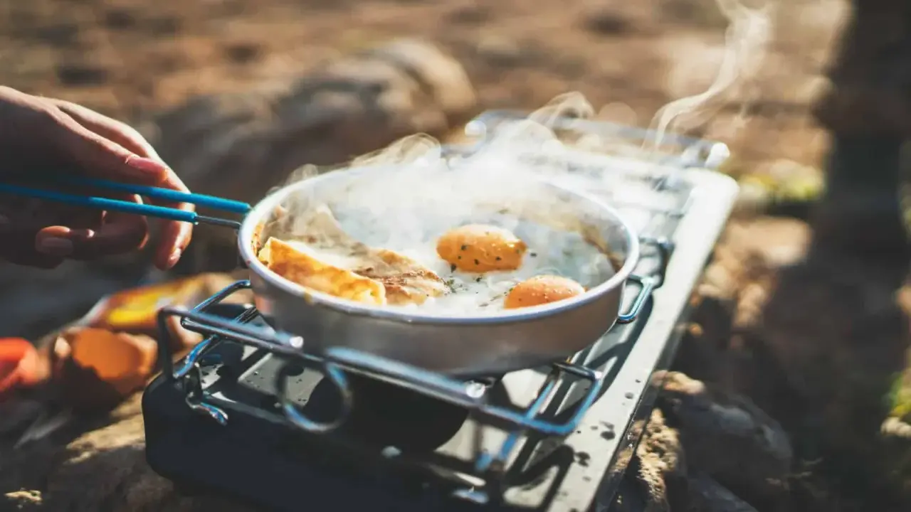 Spiegeleier und Brot brutzeln in einer Pfanne auf einem Gaskocher. Perfekte Camping Rezepte für unterwegs.
