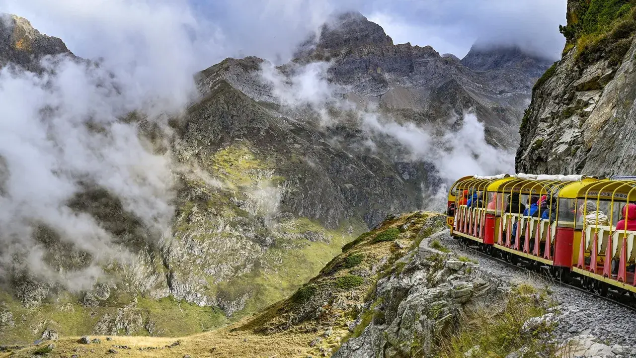 Gelber Zug fährt durch neblige Berglandschaft in den Pyrenäen, Frankreich.