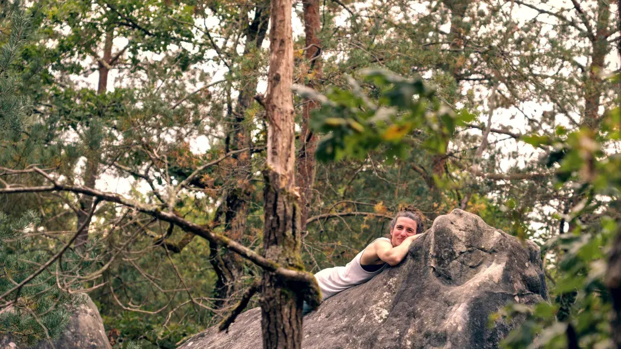 Frau ruht sich nach dem Fontainebleau Bouldern auf einem Felsen aus, umgeben von Bäumen.