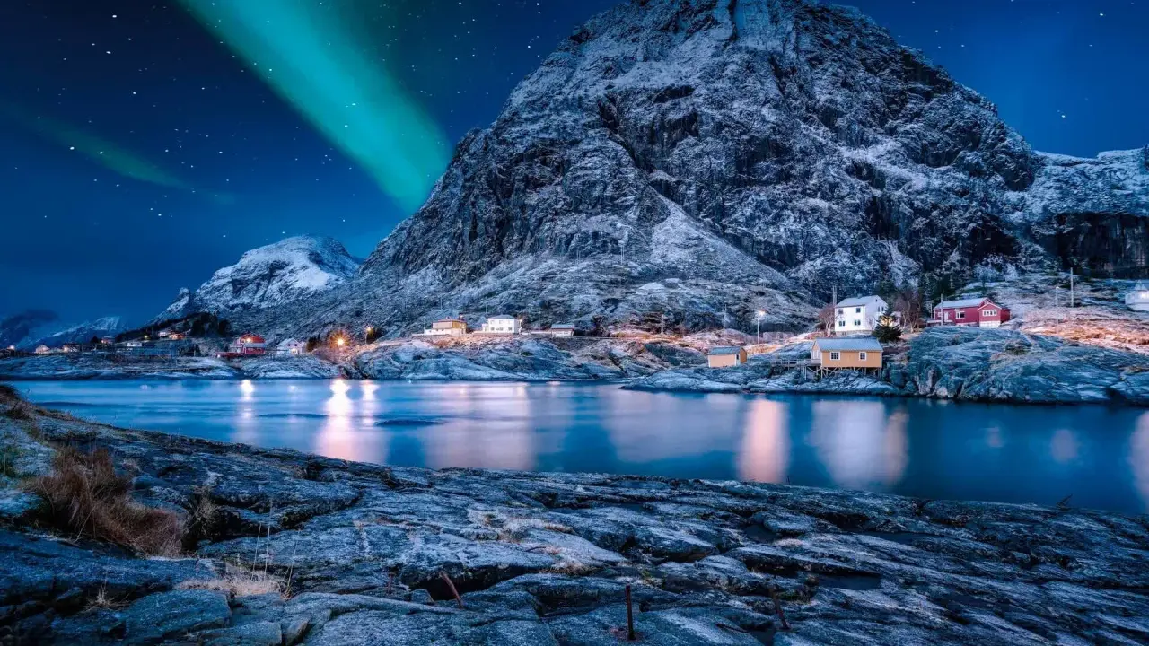Ein malerisches Dorf in Norwegen im Winter, beleuchtet von den Nordlichtern und dem Sternenhimmel.