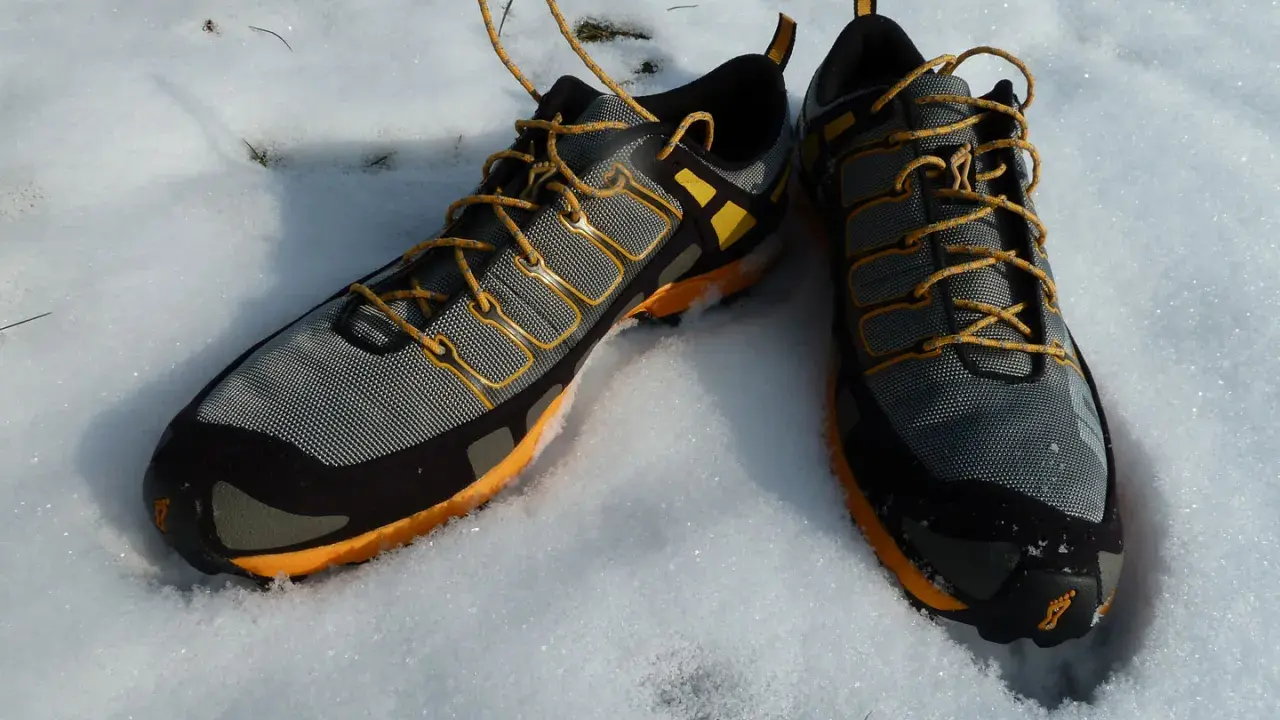 Graue und orangefarbene trailrunningschuhe zum wandern liegen im Schnee.
