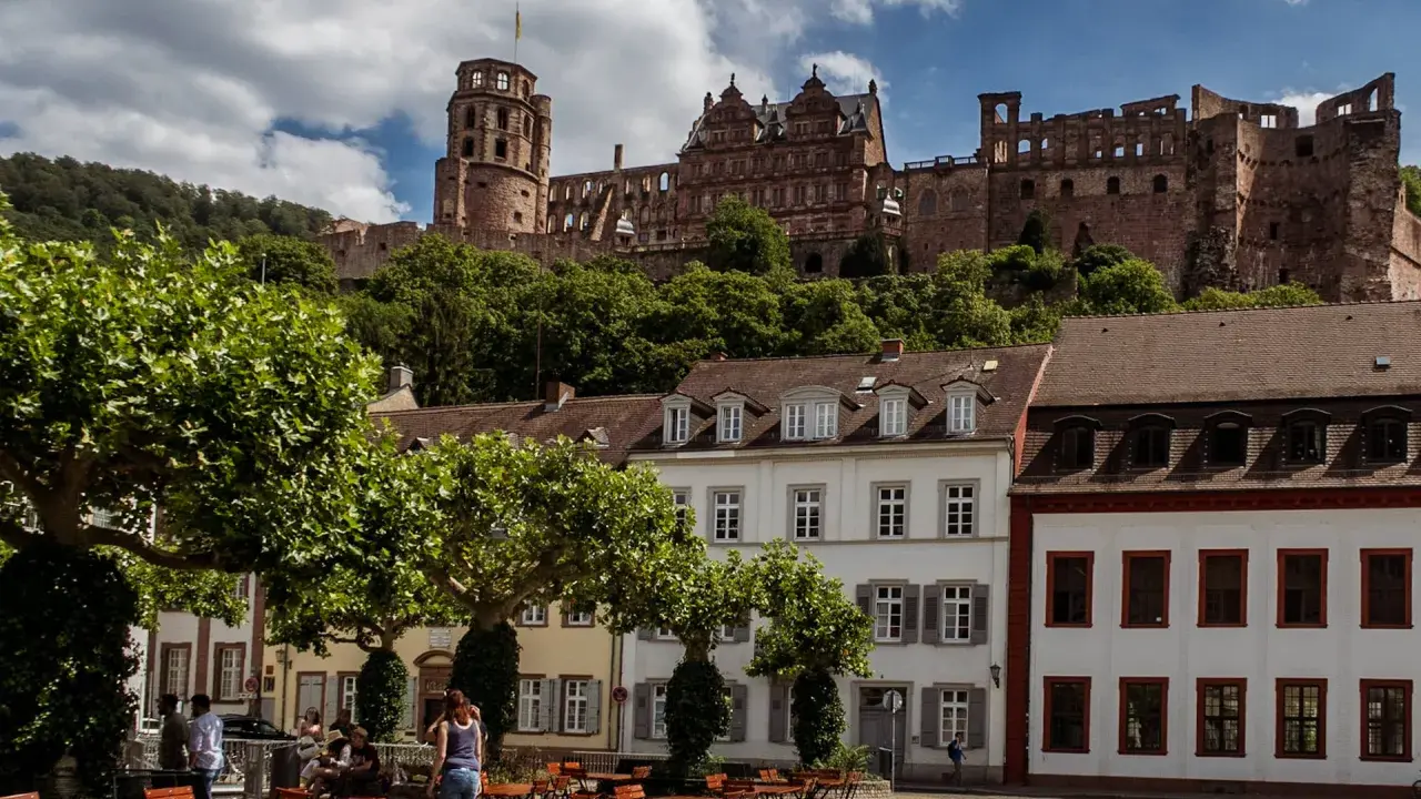 Heidelberg entdecken: Majestätisches Schloss thront über malerischen Häusern und grünen Bäumen. Ein idyllischer Platz lädt zum Verweilen ein.