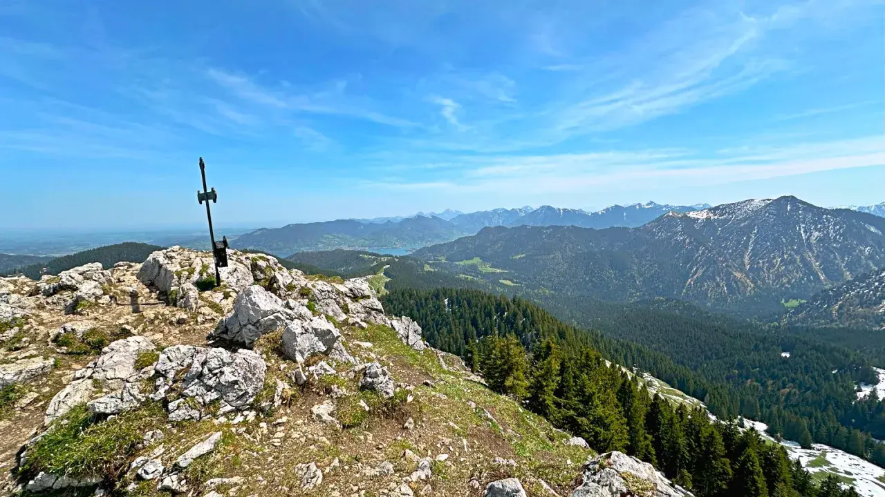 Gipfelkreuz am Fockenstein bei Lenggries, mit Blick über Wälder und Berge bis zum See.