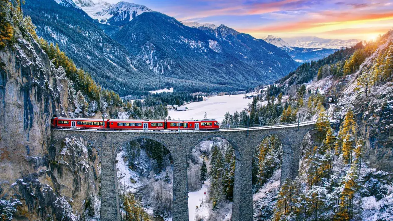 Roter Zug überquert eine Steinbrücke in verschneiter Schweizer Alpenlandschaft. Ein perfektes reiseziel schweiz.
