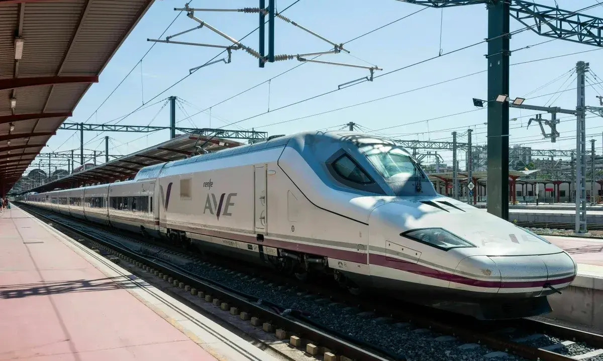 Moderner, weißer Renfe ave zug mit lila Akzenten steht auf Gleisen unter einem Bahnhofsdach.