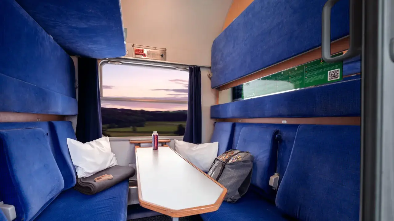Gemütliche Kabine im Holland Zug mit blauen Sitzen, einem Tisch und Blick auf die Landschaft bei Sonnenuntergang.