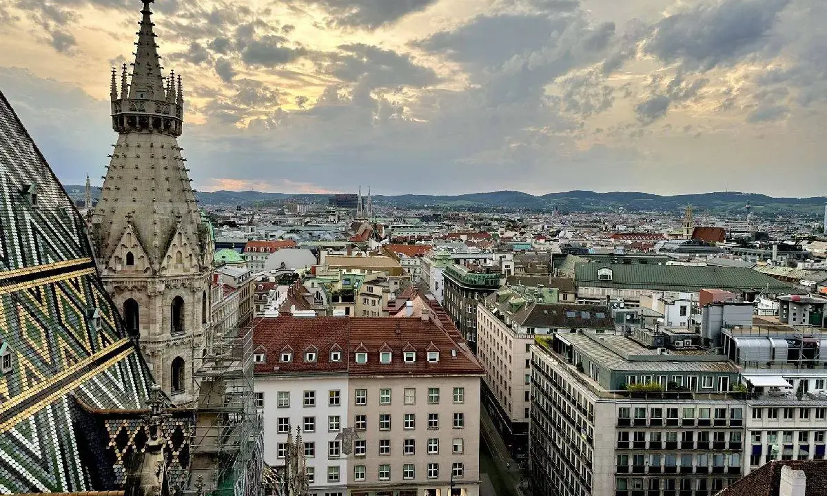 Blick über die Dächer Wiens bei Sonnenuntergang. Ein Turm des Stephansdoms ragt empor. Ein perfekter Moment, um Wien zu erleben.