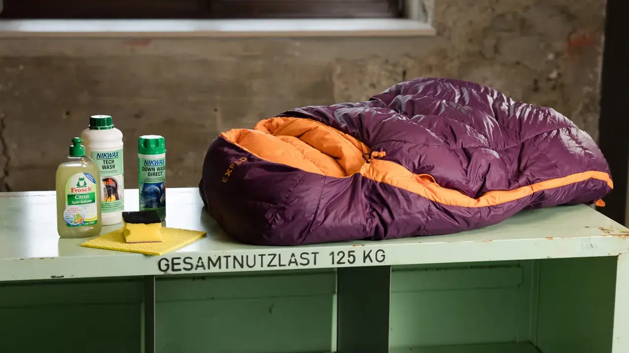Lila-orangefarbener Exped-Schlafsack bereit zum Schlafsack waschen, daneben Reinigungsmittel und Schwamm.