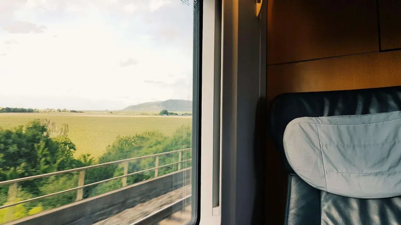 Blick aus dem Zugfenster auf grüne Felder und Hügel. Bequemer Sitzplatz im Abteil, bereit für die Reise durch den Euro city.