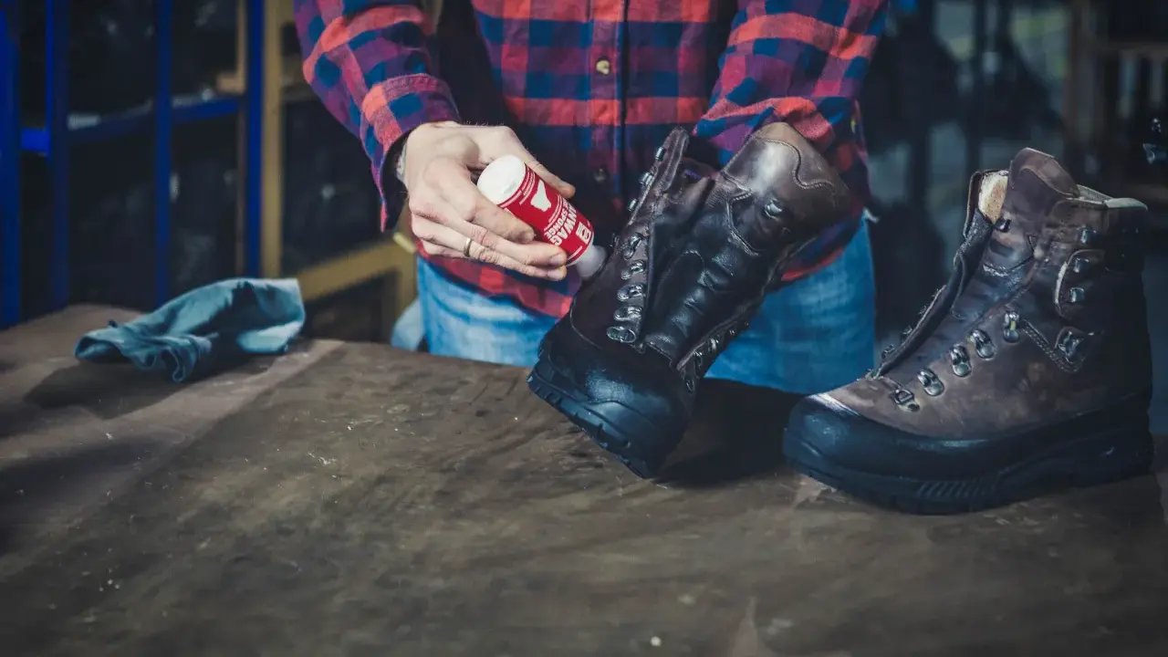 Mann pflegt Hanwag Schuhe mit einem roten Pflegeprodukt. Ein blaues Tuch liegt daneben.
