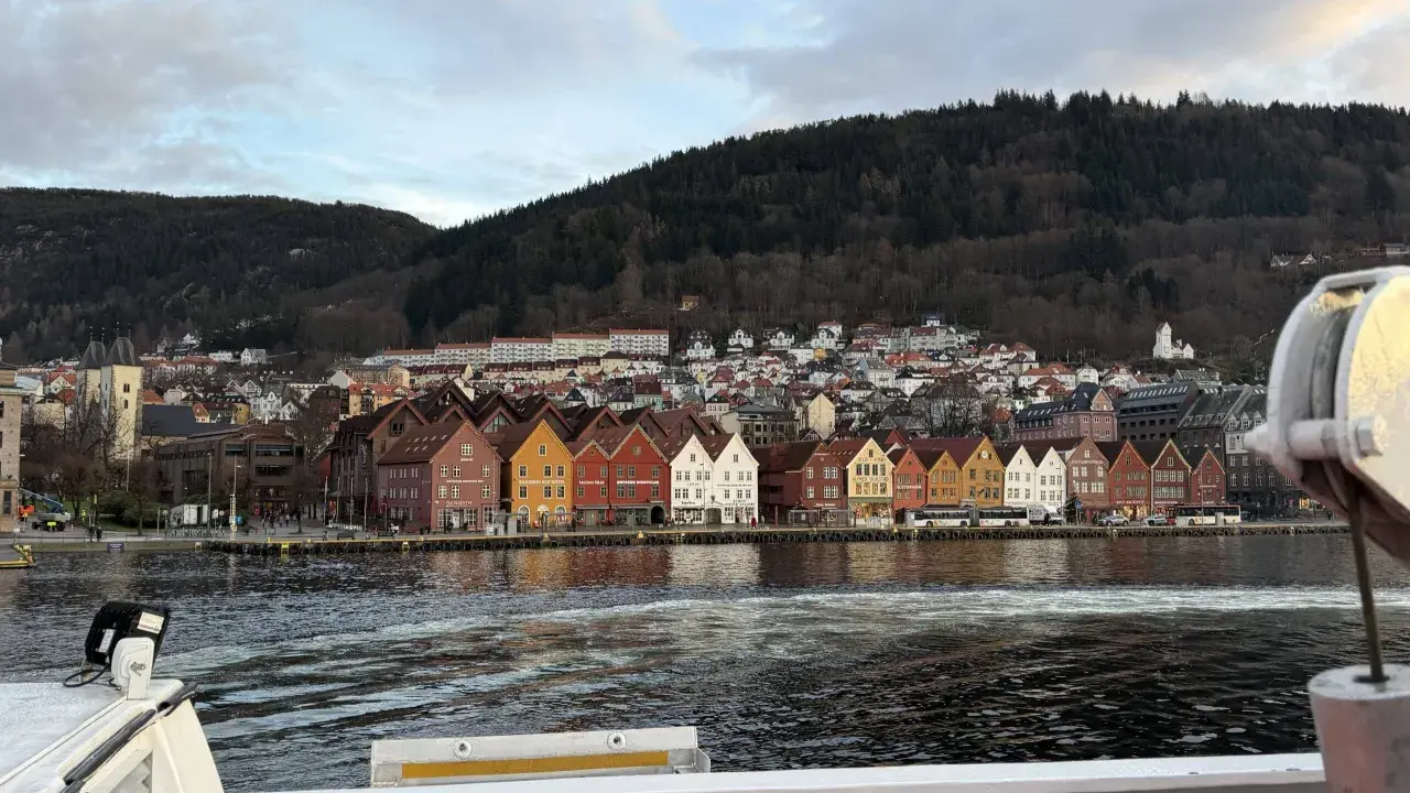 Bunte Holzhäuser am Kai von Bergen, mit einem bewaldeten Hügel im Hintergrund. Die bergen bahn ist hier nicht zu sehen, aber die Aussicht ist malerisch.
