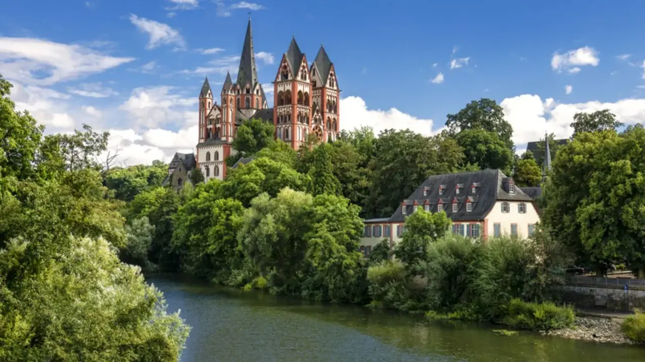 Ein malerischer Blick auf den Limburger Dom, umgeben von üppigem Grün und dem Fluss Lahn. Perfekt für einen Urlaub in Hessen.