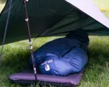 Ein dunkelblauer Kunstfaser-Schlafsack liegt auf einer Isomatte unter einem Tarp. Perfekt für Outdoor-Abenteuer, auch wenn man ihn mal waschen muss.