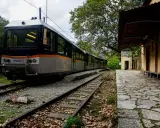 Ein Zug nach Griechenland steht auf den Gleisen neben einem alten Bahnhofsgebäude. Herbstlaub bedeckt den Bahnsteig.