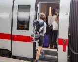 Reisende steigen in den ICE ein, um die ICE strecken zu befahren. Ein junger Mann mit Rucksack und Schuhen am Gepäck steigt als Erster ein.