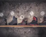 Fünf Wanderschuhe verschiedener Kategorien, darunter Kategorie B, stehen auf einem Regal vor einer Steinwand.