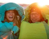 Glückliches Paar in Schlafsäcken bei Sonnenuntergang. Die Frage welcher Schlafsack bei welcher Temperatur ist hier wohl gelöst!