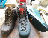 Drei Wanderschuhe von verschiedenen Herstellern: braun, grau und türkis. Werkzeuge und Garn liegen daneben.