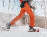 Person beim Schneeschuhwandern, die mit ihren speziellen Schuhen durch tiefen Schnee stapft.