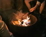 Kinder machen Feuer und rösten Würstchen über der Flamme.