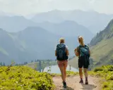 Zwei Wanderinnen genießen die Aussicht auf den **rundwanderwege Oberstdorf**. Ein Bergsee liegt im Tal, umgeben von sanften Hügeln und majestätischen Gipfeln.