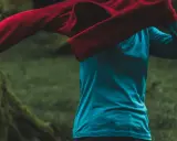 Person zieht ein rotes Oberteil über ein blaues Funktionsshirt. Das blaue Shirt ist ein Baselayer, der die Körperwärme reguliert.