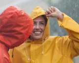 Zwei lachende Personen im Regen, eine in Gelb, die andere in Rot. Die gelbe Regenjacke ist im Fokus.