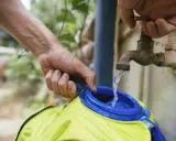 Wasser fließt aus einem alten Wasserhahn in eine gelbe Trinkblase. Nach dem Befüllen muss die Trinkblase trocknen.
