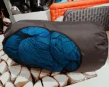 Ein blauer Schlafsack wird in einen dunklen Packsack gestopft, bereit für das nächste Abenteuer.