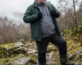 Mann in grüner Softshelljacke und grauer Kapuzenjacke wandert durch felsiges Gelände.