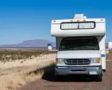 Weißer Freeway Camper steht am Straßenrand in karger Landschaft mit Bergen am Horizont.