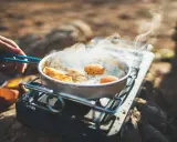 Spiegeleier und Brot brutzeln in einer Pfanne auf einem Gaskocher. Perfekte Camping Rezepte für unterwegs.