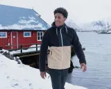 Mann in warmer Fleecejacke, bereit für das Waschen, steht vor einem roten Haus am Meer.