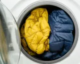 Zwei Daunenjacken, eine gelbe und eine blaue, warten darauf, in der Waschmaschine gewaschen zu werden.