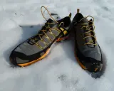Graue und orangefarbene trailrunningschuhe zum wandern liegen im Schnee.