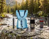 Outdoor-Ausrüstung für einen Wasserfilter-Test am Fluss: Filter, Beutel und Trinkflaschen auf einem Felsen.